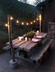 a wooden table with candles and plates on it in front of some lights hanging from the trees