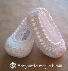 two crocheted white baby shoes sitting on top of a brown table next to each other