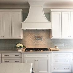 a kitchen with white cabinets and marble counter tops, an oven hood over the stove