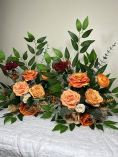 an arrangement of orange and red flowers on a white table cloth with greenery in the background