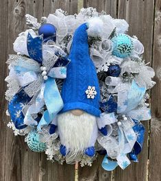 a blue and white wreath with a gnome's head on it, sitting in front of a wooden fence