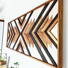 a wooden wall hanging on the side of a white wall next to potted plants