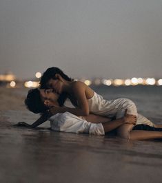 two people sitting on the beach with their arms around each other and one person kissing