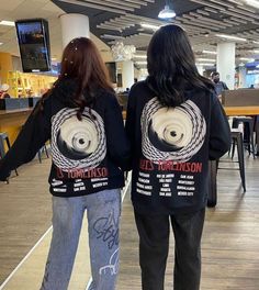 two people standing in an airport with their back to the camera, wearing black sweatshirts and jeans