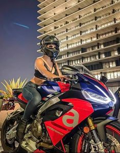 a woman sitting on top of a red and blue motorcycle in front of a tall building