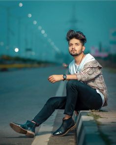 a man sitting on the side of a road with his legs crossed and looking at the camera