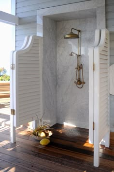 an open shower door in a bathroom with white walls and wood flooring on the outside