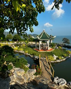 a gazebo sitting on top of a lush green field next to the ocean and trees