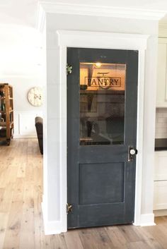 an empty kitchen with a gray door and white cabinets in the back ground, next to a wooden floor