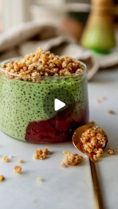 a bowl filled with fruit and granola on top of a white table next to a spoon