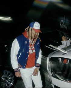 a man with dreadlocks standing next to a white car