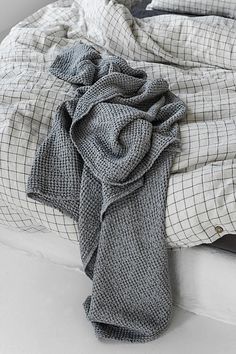 an unmade bed with grey and white sheets