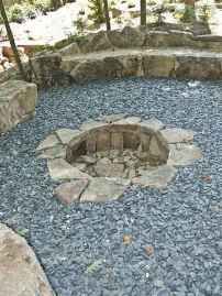 an outdoor fire pit surrounded by rocks and gravel with trees in the backround