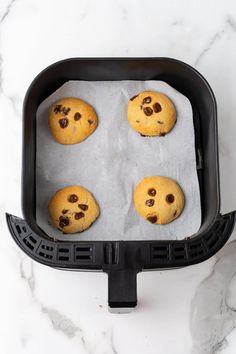 four chocolate chip cookies on a baking sheet in an air fryer with parchment paper