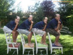 four men sitting on chairs in the grass with their hands to their chins and looking at the camera