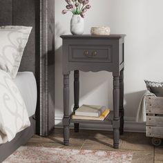 a nightstand with flowers on top of it next to a bed