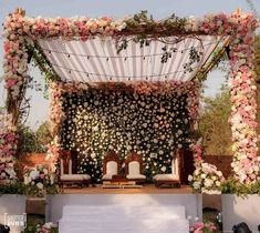 an outdoor wedding setup with white and pink flowers on the wall, two chairs at the end of the aisle