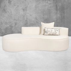 a white couch sitting on top of a floor next to a cement wall with a pillow