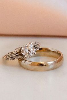 two gold wedding rings sitting on top of a white table next to a pink pillow