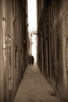 two people walking down an alley way in the middle of town with no one on it