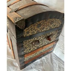 an old wooden chest with ornate designs on the top and sides, sitting on a white sheeted surface