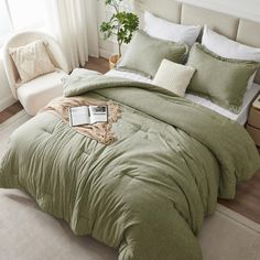 a bed with green comforter and pillows in a room next to a chair, potted plant and window