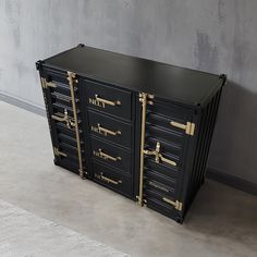 a large black cabinet with gold handles on the top and bottom, in front of a concrete wall