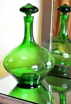 two green glass vases sitting on top of a table next to a mirror with reflection in it