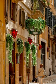 a woman walking down the street in front of a building with plants growing on it