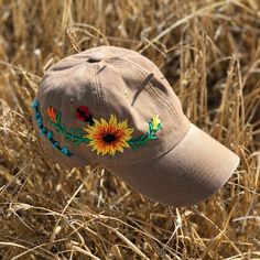 a tan hat with sunflowers and ladybug embroidered on it in a field