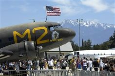 a crowd of people standing next to an airplane on top of a tarmac with mountains in the background