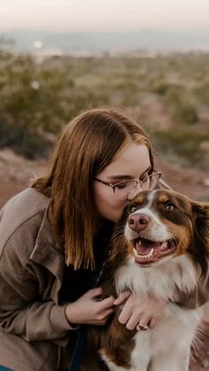 a woman is petting her dog outside in the desert with mountains in the background