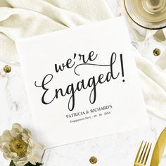 we're engaged card on a table with flowers and napkins next to it