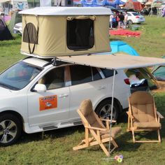 a car with a tent attached to the roof and two chairs in front of it