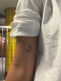 a person wearing a white shirt with a small tattoo on their arm and the moon behind them