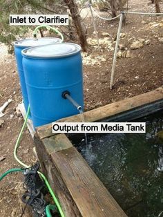 two blue barrels sitting next to each other on top of a wooden platform in the woods