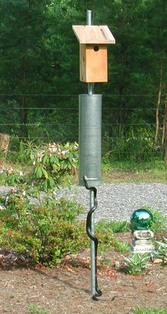 a bird house on top of a pole in the grass next to some bushes and trees