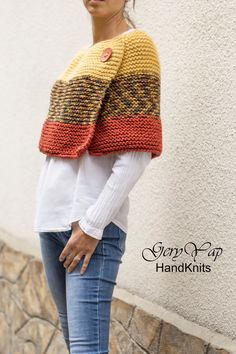 a woman standing next to a white wall wearing a yellow and red knitted shawl