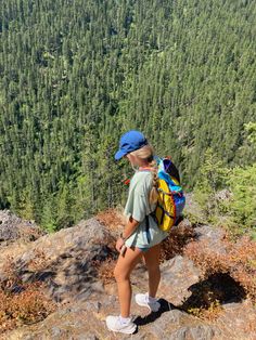 a woman standing on top of a mountain looking down at the trees and mountains behind her