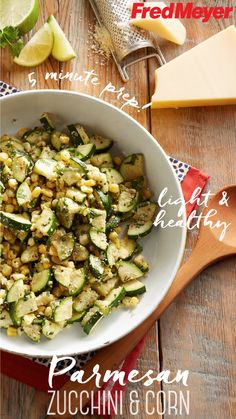 a bowl filled with zucchini and corn on top of a wooden table next to cheese