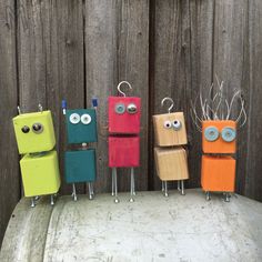 four different colored toy robots standing in front of a wooden fence with eyes on them