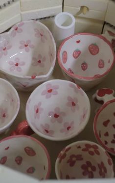 pink and white bowls with strawberries on them are sitting in a bowl filled with water