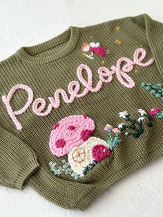 a green sweater with pink flowers and the word prensee written in large letters