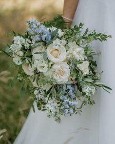 a bridal holding a bouquet of white and blue flowers in her hands with greenery