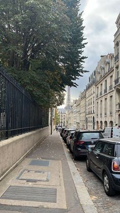 cars parked on the side of a street in front of tall buildings with iron fences