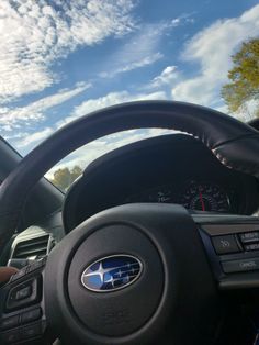 the steering wheel and dashboard of a car on a sunny day with clouds in the sky