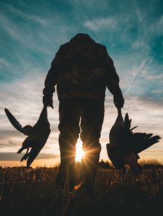 the silhouette of a man holding two birds in his hands, with the sun shining behind him