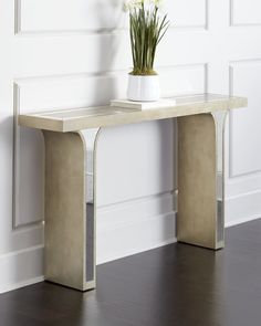 a white vase with flowers sitting on top of a wooden table next to a wall