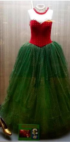 a green and red dress on display in a glass case next to a gold shoe