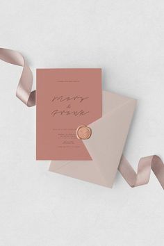 a pink and gold wedding card with a ring on it next to a satin ribbon